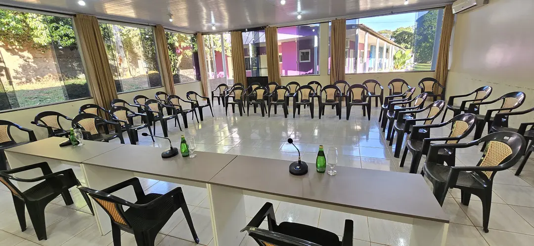 Sala de reunião executiva com mesas em U, microfones e janelas para o jardim