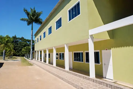 Fachada do bloco de suítes de dois andares, com palmeira e céu azul