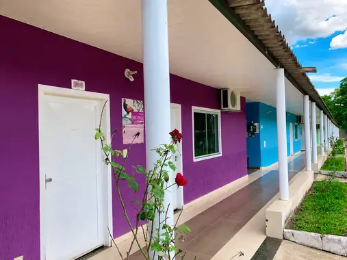 Corredor dos chalés coloridos, com paredes roxa e azul, colunas brancas e roseiras