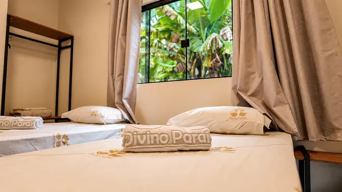 Toalha e roupa de cama com a marca Divino Paraíso, e janela para as bananeiras