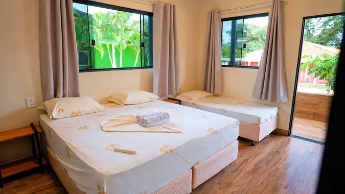 Suíte clara com cama de casal e cama de solteiro, janelas para as palmeiras
