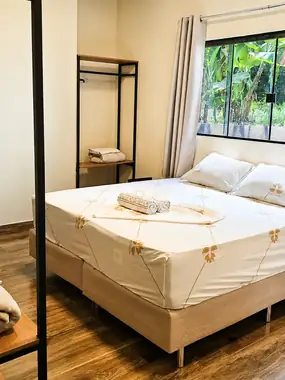 Suíte com cama de casal, toalhas dobradas e janela para o verde