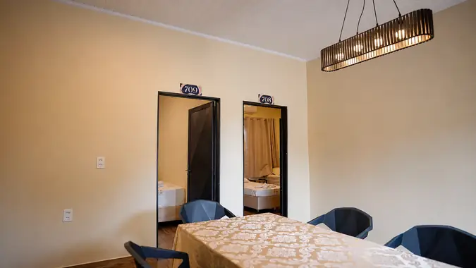 Sala com mesa e cadeiras sob luminária pendente, entre as portas de duas suítes