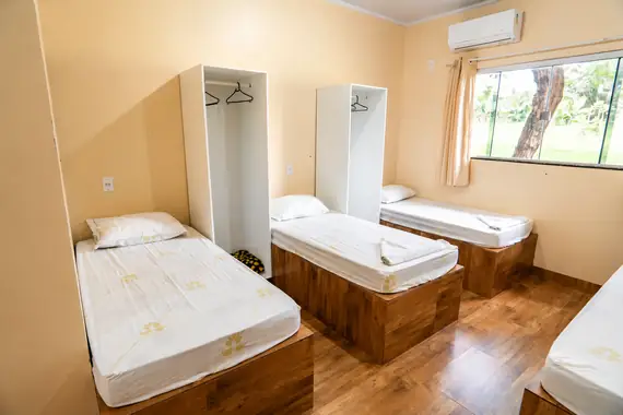Suíte com camas de solteiro, armários, ar-condicionado e janela para o gramado