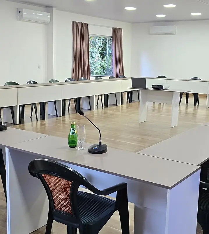 Sala de reunião clara com mesas brancas em U e microfones